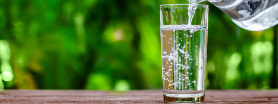 Water in jug poured into glass on wood with nature background. World Water Day