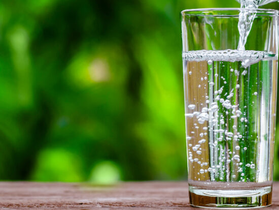 Water in jug poured into glass on wood with nature background. World Water Day