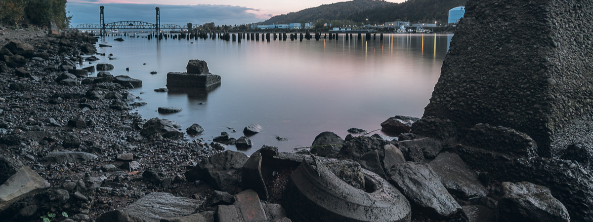 The rocky bank of the Willamette River near St. John's. The train bridge is in the distance and an old tire blends in with the rocks Superfund cleanup