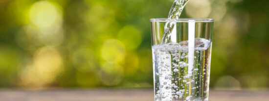 Water in jug poured into glass on wood with nature background. World Water Day