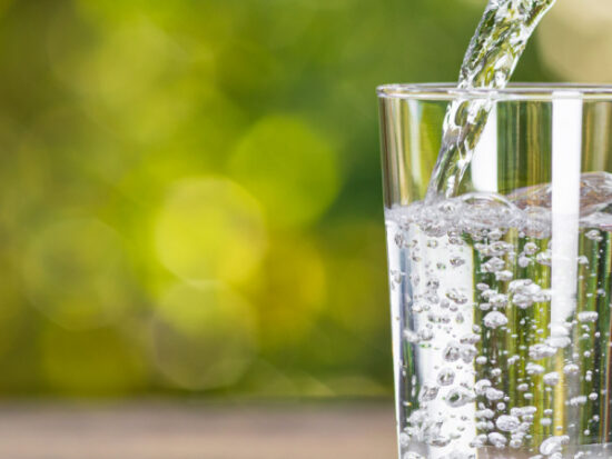 Water in jug poured into glass on wood with nature background. World Water Day